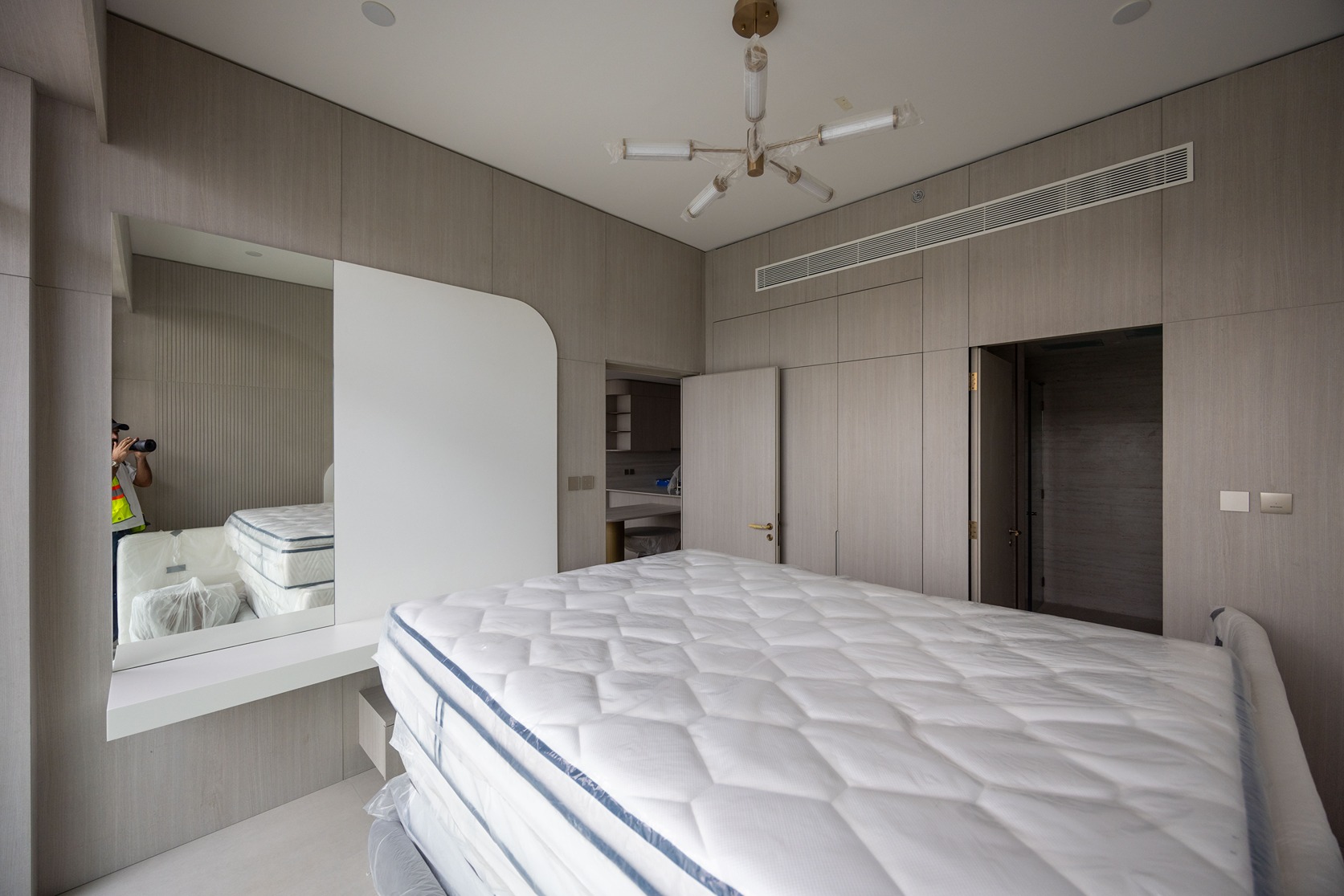 Pearl House By Imtiaz A modern bedroom featuring a newly placed mattress, wooden walls, and a mirror reflecting part of the room.